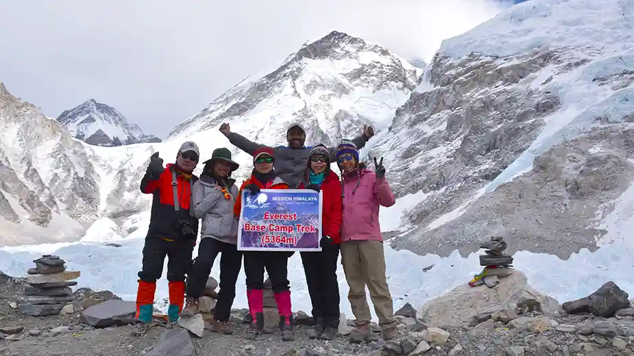 Group celebrating their victory at Everest Base Camp, holding a banner with stunning Himalayan peaks in the background